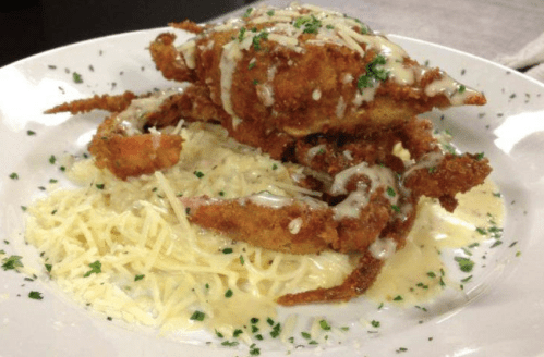 A plate of fried crab atop creamy pasta, garnished with parsley and drizzled with a white sauce.