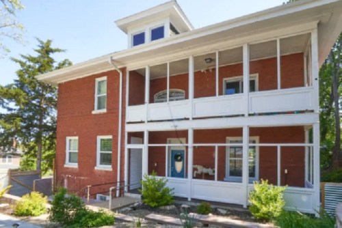 A two-story red brick house with white trim, featuring a porch and landscaped front yard.