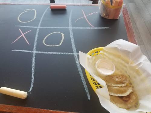 A chalkboard with a tic-tac-toe game and a basket of fried dumplings with dipping sauce on a table.