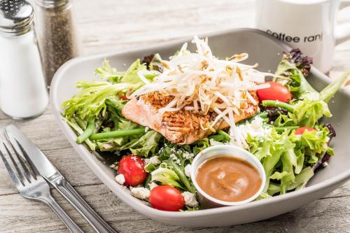 A fresh salad topped with grilled salmon, cherry tomatoes, and sprouts, served with a side of dressing.
