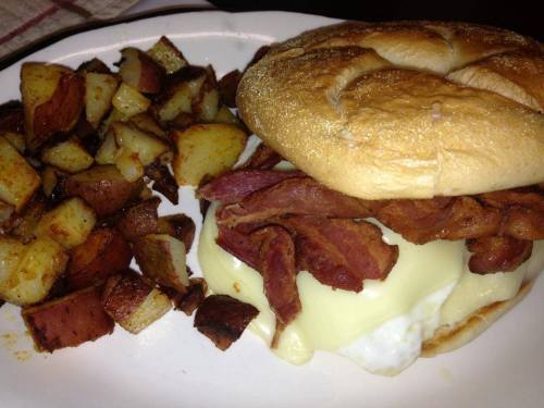 A plate featuring a sandwich with bacon and melted cheese, alongside crispy roasted potatoes.