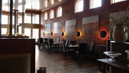 Interior of a restaurant featuring brick walls, wooden floors, and elegant seating with artwork and ambient lighting.