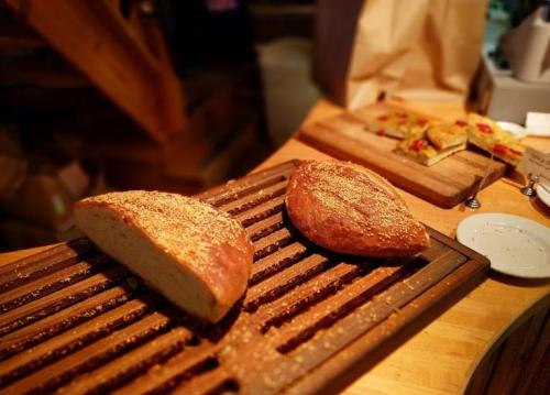 Two loaves of freshly baked bread on a wooden cutting board, with one loaf partially sliced and sprinkled with sesame seeds.