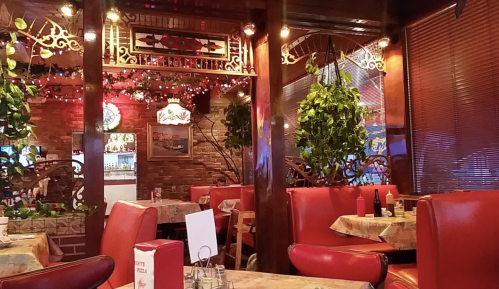 Cozy restaurant interior with red booths, wooden decor, and plants, featuring tables set for dining.
