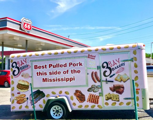 Food truck with a colorful sign advertising "Best Pulled Pork this side of the Mississippi" and various food images.