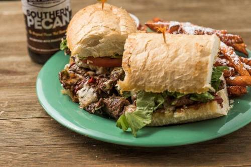 A close-up of a sandwich with meat, lettuce, and tomato on a green plate, alongside sweet potato fries and a drink.
