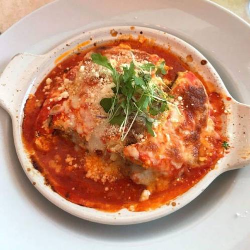 Baked lasagna in a white dish, topped with melted cheese, herbs, and a rich tomato sauce.