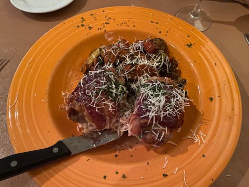 A vibrant orange plate with two meat rolls topped with cheese, served alongside a medley of roasted vegetables.