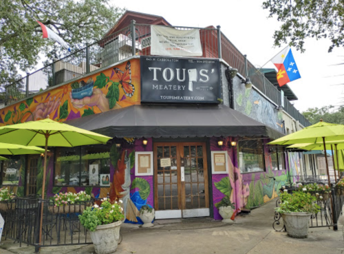 Colorful exterior of Tout's Eatery with vibrant murals, outdoor seating, and a Texas flag.