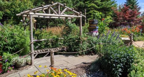 A rustic wooden arbor surrounded by vibrant flowers and greenery in a sunny garden setting.
