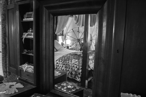 A vintage wooden mirror reflecting a cozy bedroom with a quilted bed and decorative items.