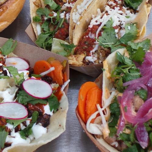 A close-up of colorful tacos and bowls filled with fresh ingredients like cilantro, radishes, and carrots.