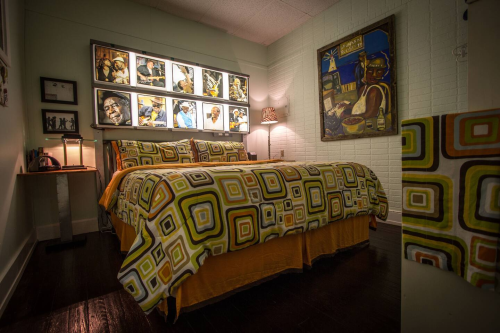 Cozy bedroom featuring a colorful patterned bedspread, framed artwork on the walls, and warm lighting.