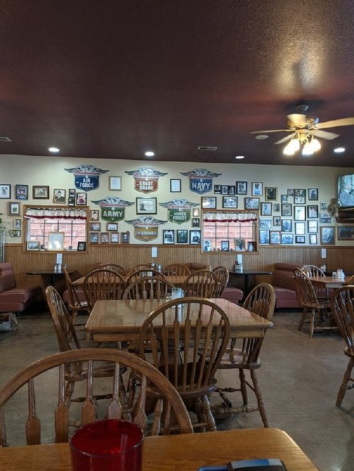 Interior of a cozy restaurant with wooden tables, chairs, and walls adorned with military memorabilia and framed photos.