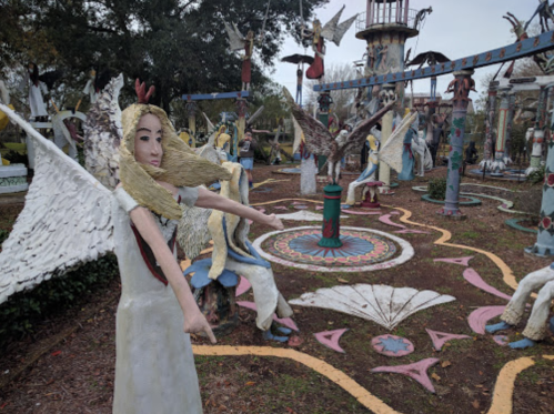 A whimsical outdoor art installation featuring colorful sculptures of angels and other figures in a garden setting.