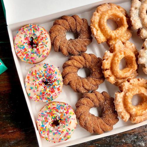 A box of assorted donuts, including frosted with sprinkles, cinnamon twists, and glazed varieties.