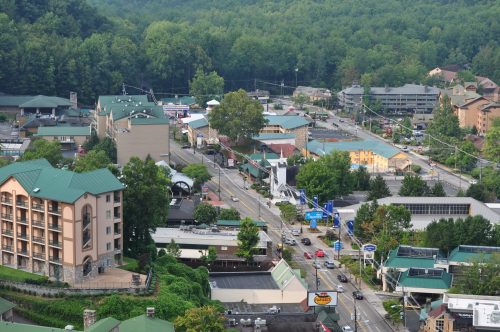 Aerial view of a small town with green-roofed buildings, trees, and a road lined with cars.