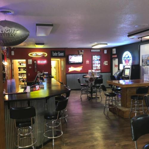 Interior of a bar with a wooden counter, stools, a TV, and a cozy atmosphere.