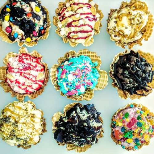 A colorful assortment of ice cream sundaes in waffle bowls, topped with various candies, sauces, and sprinkles.