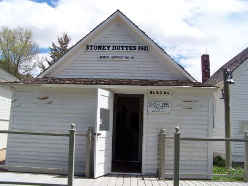 Historic Stoney Buttes schoolhouse, built in 1911, with a white exterior and a sign indicating its school district.