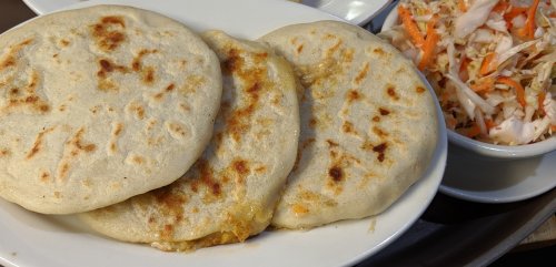 Three golden-brown pupusas served on a plate, accompanied by a side of coleslaw.