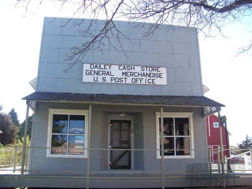 A gray building with a sign reading "Dailey Cash Store, General Merchandise, U.S. Post Office" and large windows.