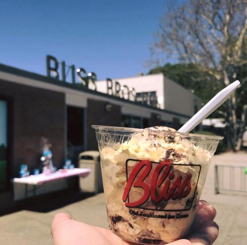 A hand holding a cup of ice cream in front of a shop sign that reads "Bliss Old-Fashioned Ice Cream."