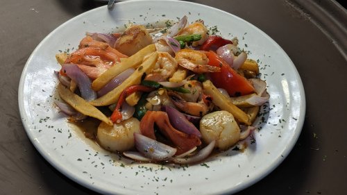A plate of colorful stir-fried shrimp and vegetables, including onions, peppers, and potatoes, garnished with herbs.