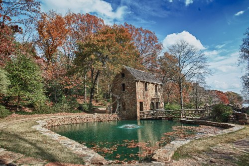 A rustic stone building by a pond, surrounded by vibrant autumn trees and a clear blue sky.
