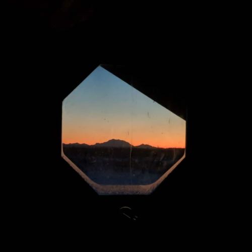 View of a mountain silhouette at sunset, framed by an octagonal window with a dark background.
