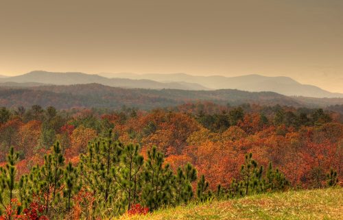 A scenic view of rolling mountains and vibrant autumn foliage under a hazy sky.