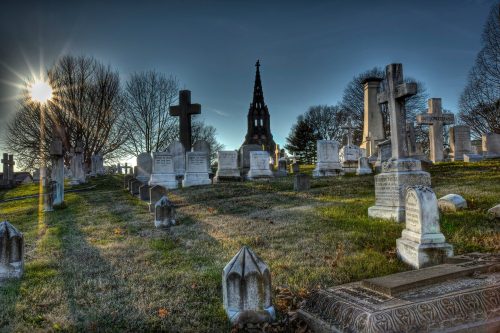 A serene cemetery at sunset, featuring various gravestones and a tall monument in the background.