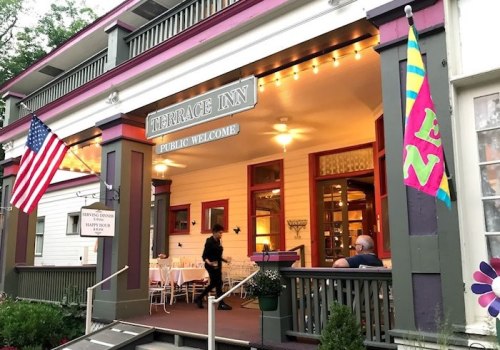 A charming inn with a welcoming porch, American flag, and colorful banners, inviting guests to enjoy the outdoor dining area.