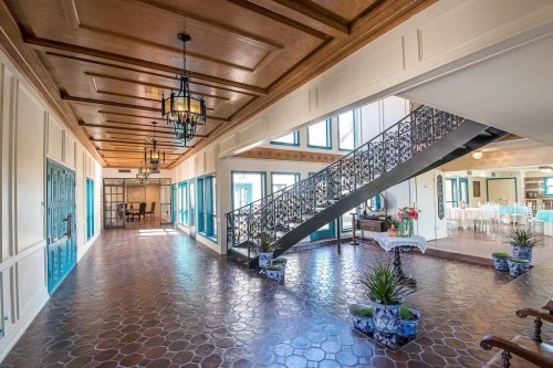 Elegant interior hallway with wooden ceiling, decorative staircase, and potted plants, leading to a dining area.
