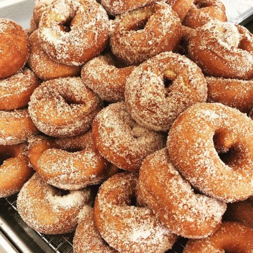 A close-up of a pile of freshly made, sugar-coated donuts on a cooling rack.