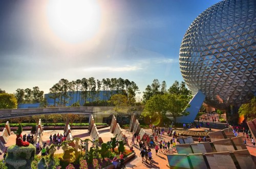 A sunny day at a theme park featuring a large geodesic dome and vibrant flower displays with visitors exploring the area.