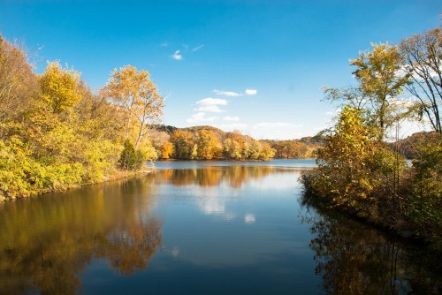 A serene lake surrounded by autumn trees, reflecting the blue sky and colorful foliage.