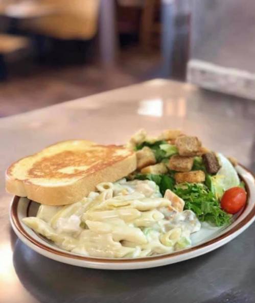 A plate of creamy pasta, a side salad with croutons, and a slice of toasted bread on a table.