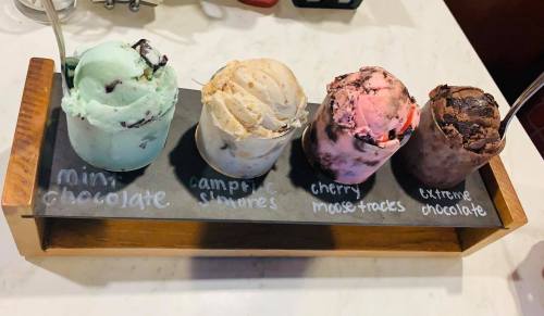 Four ice cream scoops in a wooden tray: mint chocolate, campfire s'mores, cherry moose tracks, and extreme chocolate.
