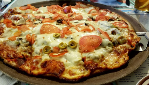 A freshly baked pizza topped with pepperoni, olives, tomatoes, and melted cheese on a round wooden platter.
