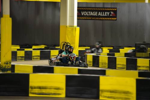 A go-kart racing on a track with yellow and black barriers in an indoor facility.