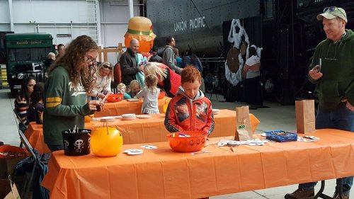 A festive gathering with children and adults at tables, crafting Halloween decorations in a decorated space.