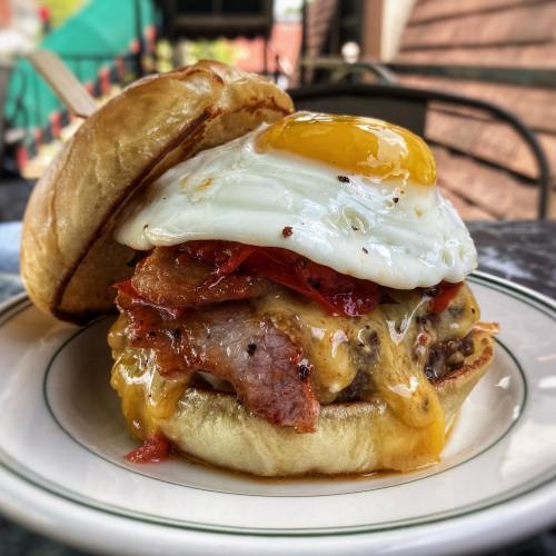 A delicious burger topped with melted cheese, crispy bacon, roasted red peppers, and a sunny-side-up egg on a toasted bun.