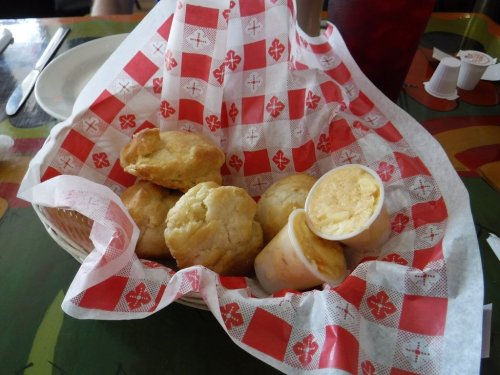 A basket of golden biscuits with two small cups of butter on a colorful table.