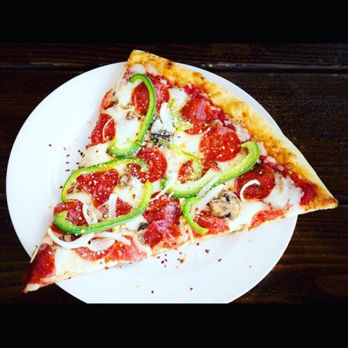 A slice of pepperoni pizza topped with green peppers, onions, and mushrooms on a white plate.