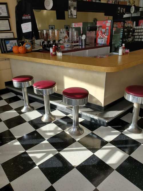 A retro diner interior featuring a counter with four red stools and a black and white checkered floor.