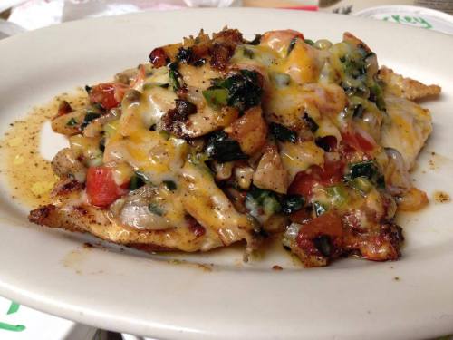 A plate of baked fish topped with melted cheese, sautéed vegetables, and herbs.