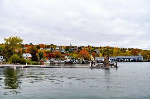 A scenic view of a waterfront town with colorful autumn trees and a cloudy sky.