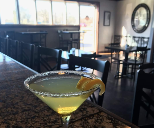A close-up of a lemon cocktail with a sugared rim, set on a bar in a cozy, empty restaurant.