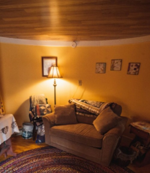 Cozy living room corner with a brown couch, lamp, and warm yellow walls, featuring a round rug and framed artwork.